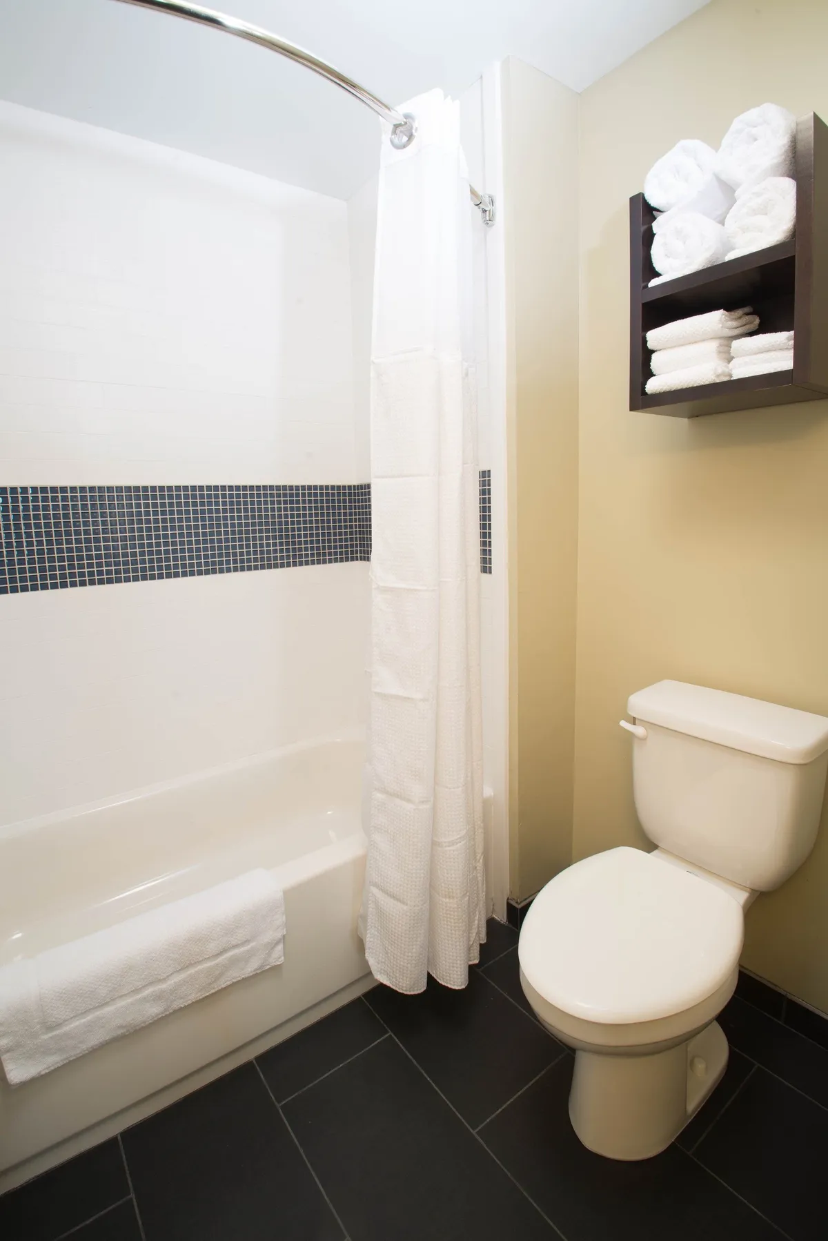 A clean and inviting bathroom with a bathtub, toilet, towel shelf, and shower curtain. The setting is calm and refreshing, ideal for unwinding after a workout or swim.