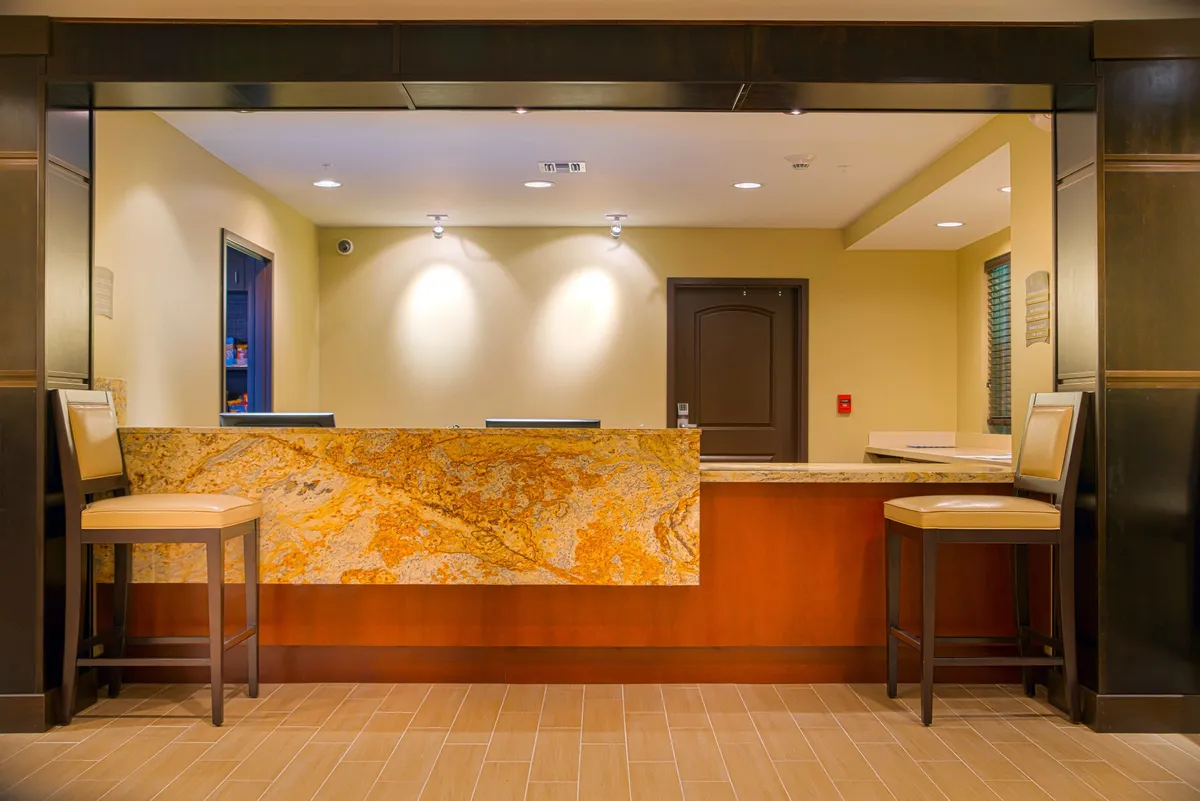 A view of the granite reception desk and surrounding seating area, providing a glimpse of the space where guests are welcomed and can casually gather. The ambiance is inviting and professional, hinting at the communal and social energy of the property.