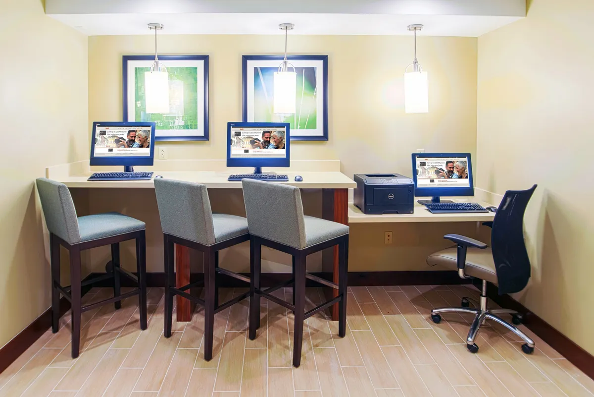 A stylish, modern interior workspace with several computers on desks, chic light fixtures, and vibrant artwork adorning the walls. Professionals are engaged in work activities, suggesting a productive environment with access to up-to-date technology.