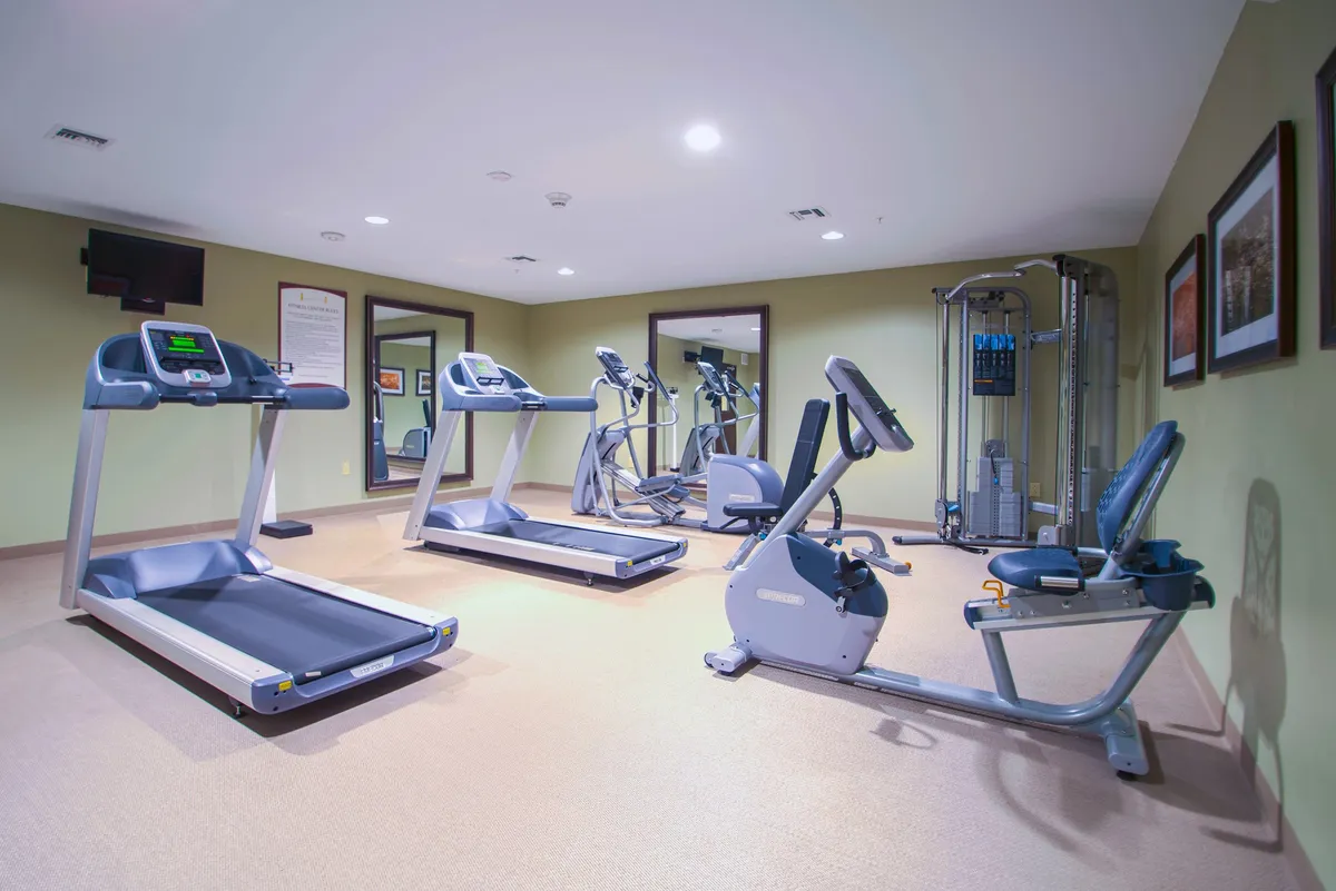 A bright, well-equipped fitness center featuring treadmills, an elliptical machine, a recumbent bike, and a weight machine. The space is designed for both individual and group workouts, with ample lighting and mirrored walls to create an energizing atmosphere.