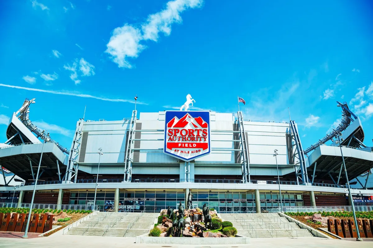 The exterior of Sports Authority Field featuring its prominent sign, a dramatic statue of football players, and steps leading to the entrance. The atmosphere is vibrant and full of anticipation, suggesting memorable outings for families, from sports events to community gatherings.