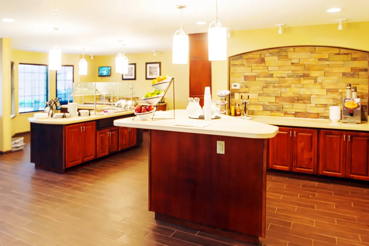 A welcoming dining area centers around a sturdy countertop adorned with a fruit display, set against a backdrop of a stone wall and warm lighting fixtures. The scene evokes a sense of gathering, socializing, and enjoying shared meals in a cozy, communal environment.